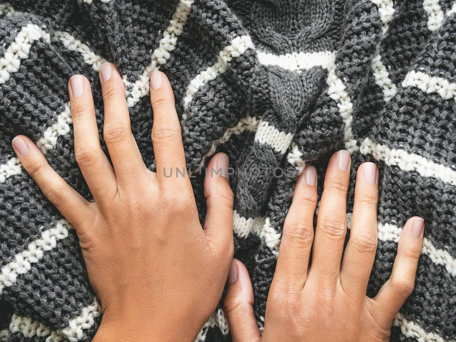 Woman's hands on gray knitted sweater with white stripes. Folded warm clothing. Crumpled textile background.