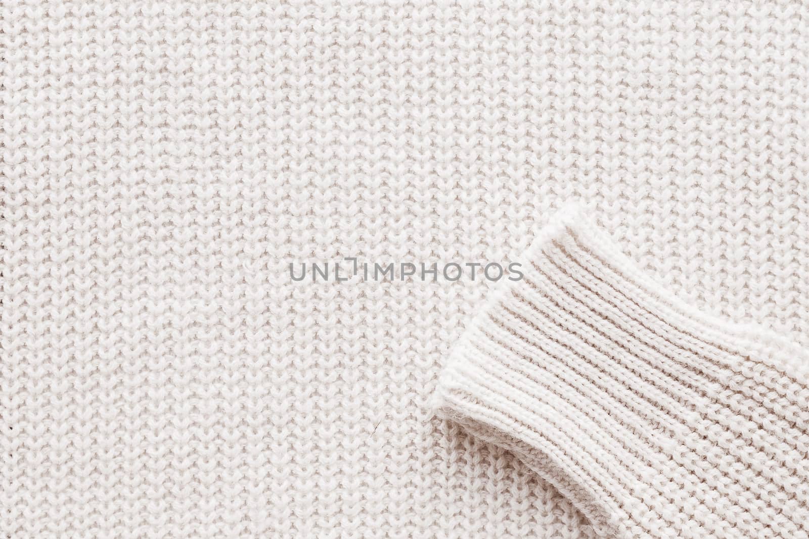 Abstract knitted background. White woolen sweater with sleeves. Close up picture of knitted pattern.