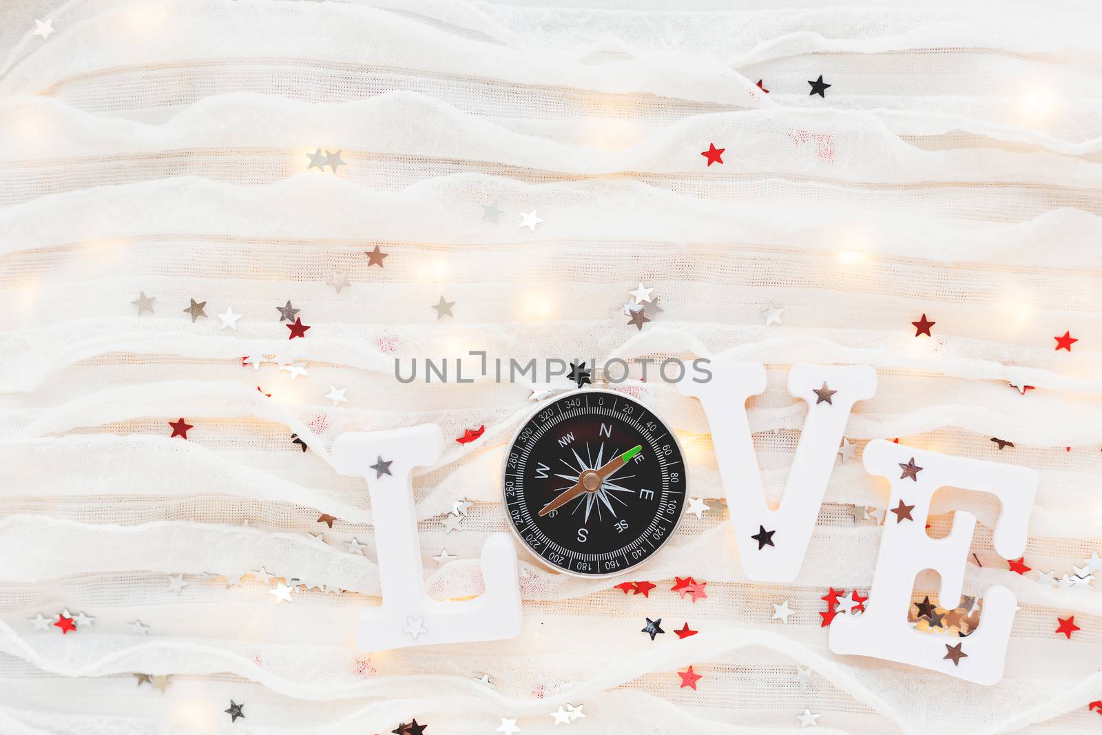 Love background. Travel symbol - compass and confetti on white fabric. Flat lay, top view.
