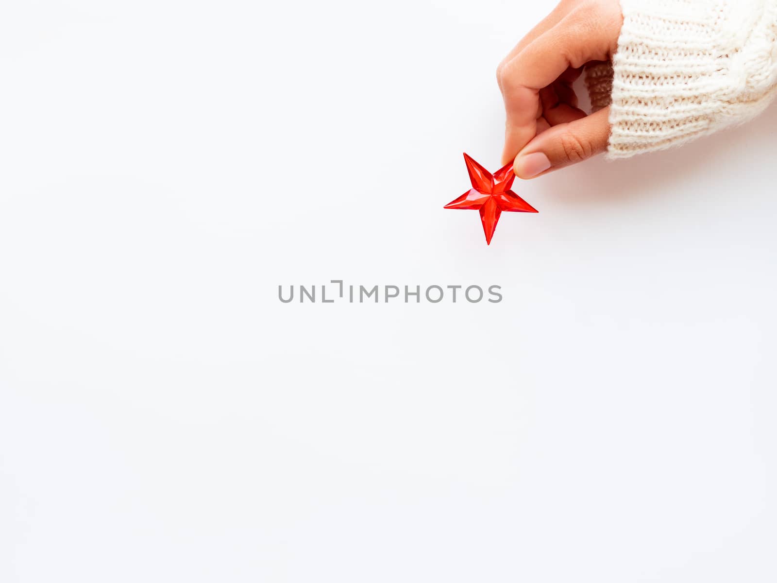 Woman in knitted sweater is holding New Year decoration - red star on white background. Top view on decoration for Christmas tree.