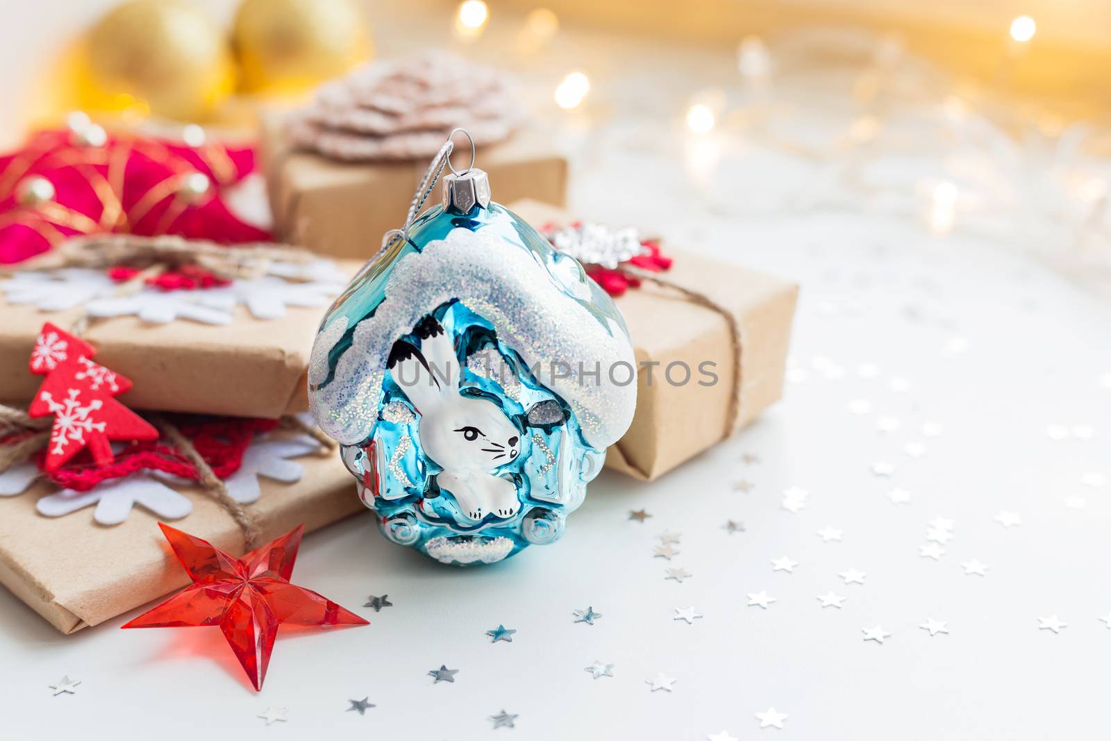 Christmas and New Year background with toy rabbit house, presents and decorations for Christmas tree. Holiday background with stars confetti and light bulbs. Place for text.