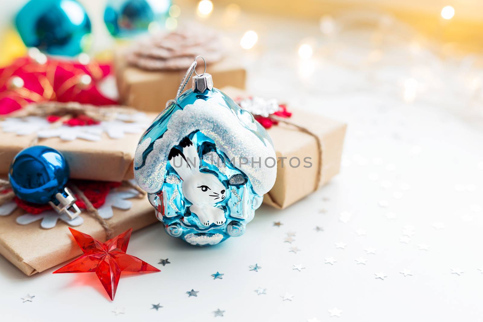 Christmas and New Year background with toy rabbit house, presents and decorations for Christmas tree. Holiday background with stars confetti and light bulbs. Place for text.