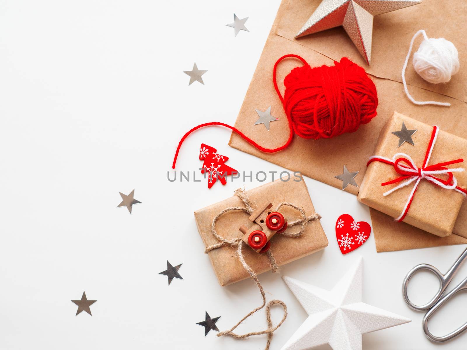 Christmas and New Year DIY presents in craft paper. Holiday gifts tied with white and red threads with toy train and red heart symbol as decoration.