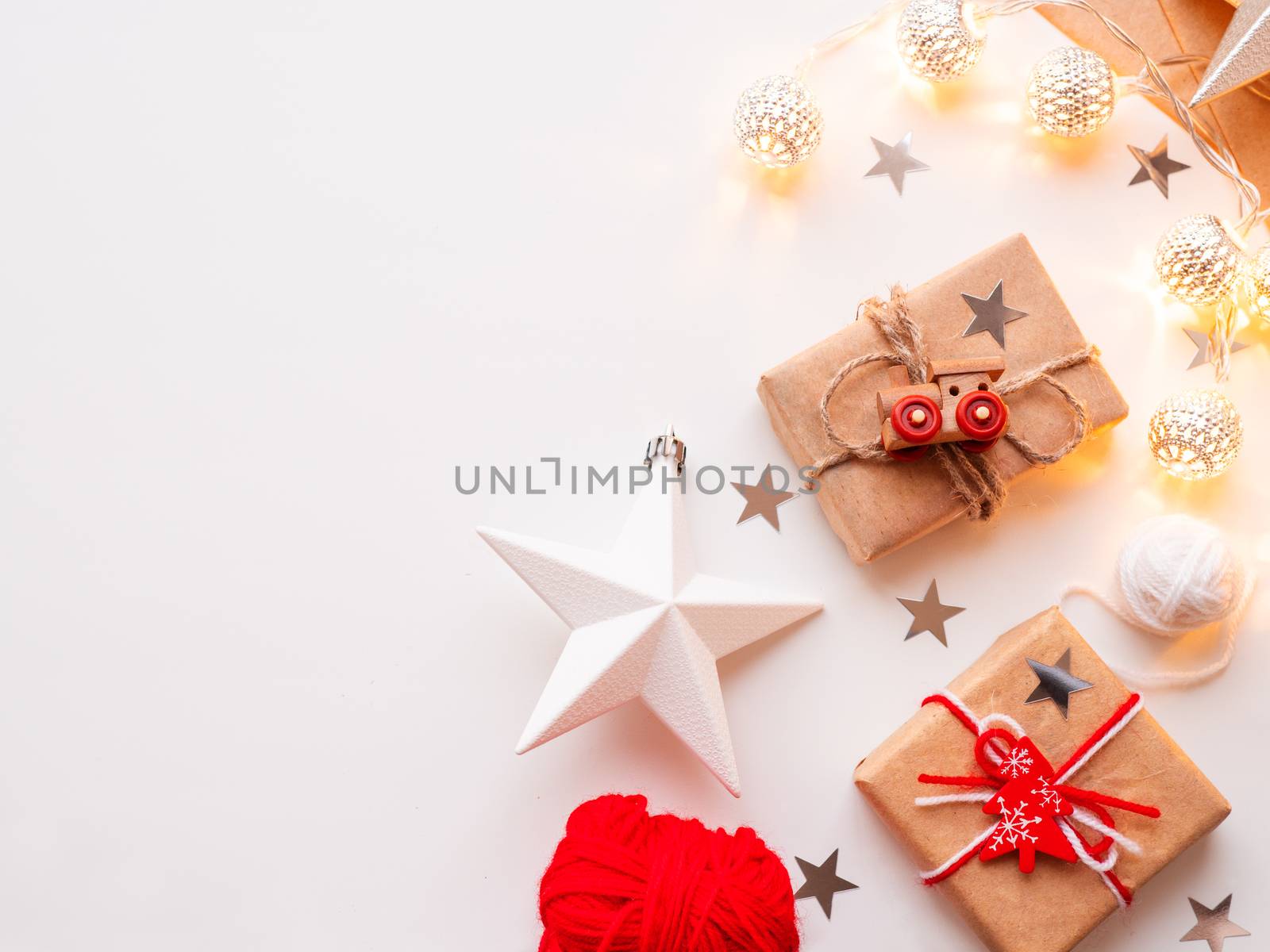 Christmas and New Year wrapped DIY presents in craft paper. Gift tied with rustic thread with toy train as decoration. Metal light bulbs with delicate pattern. Christmas tree decorations.