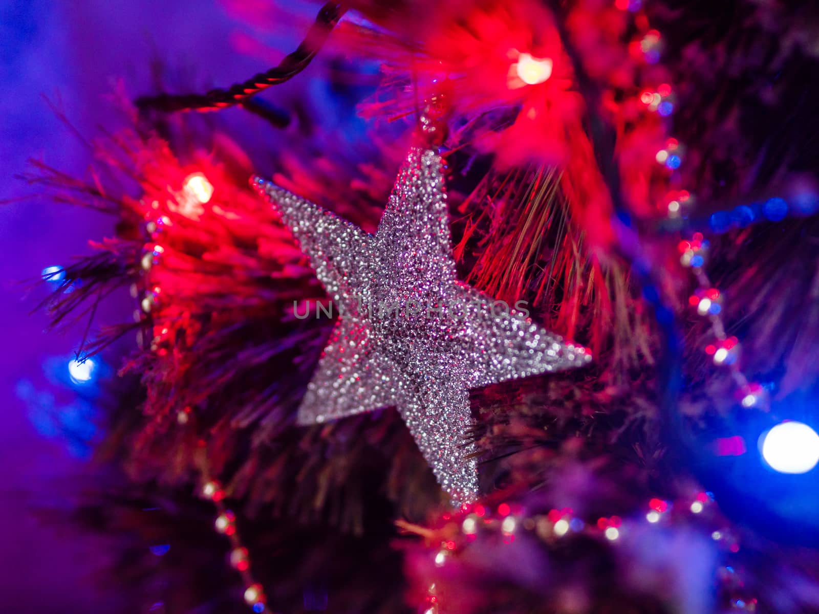 Silver sparkling star on Christmas tree. Colorful light bulbs and decorations on traditional fir tree for New Year celebration.