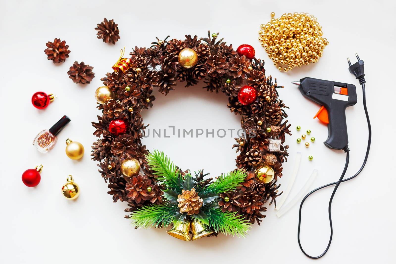 Handmade Christmas wreath and things you need to make it - pine cones, glitter, decorative balls and beads, glue gun.