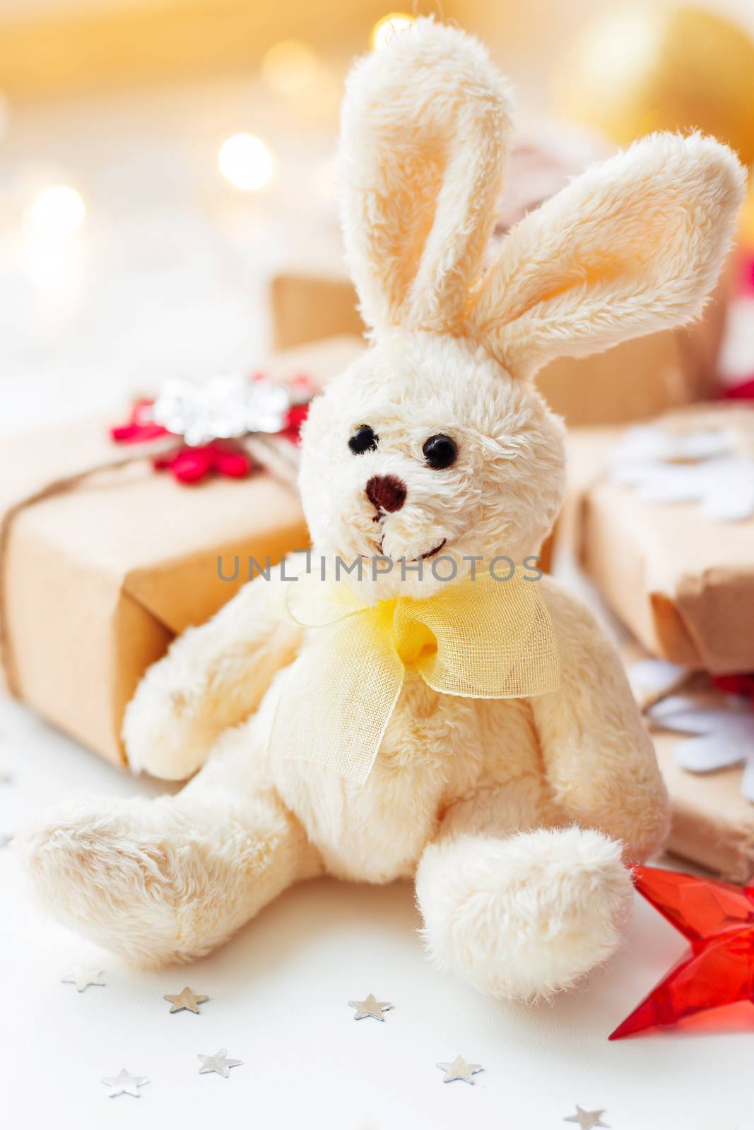 Christmas and New Year background with toy plush rabbit, presents and decorations for Christmas tree. Holiday background with stars confetti and light bulbs.