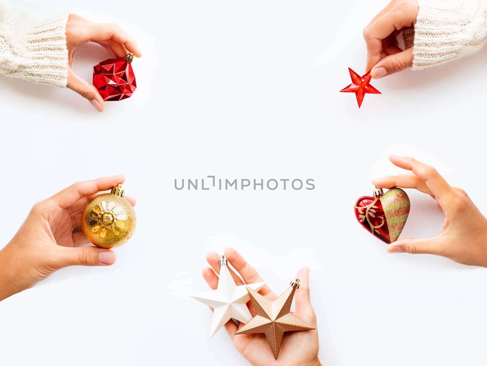 People are holding New Year decoration - balls, hearts, stars on white background. Top view on decoration for Christmas tree. Copy space.