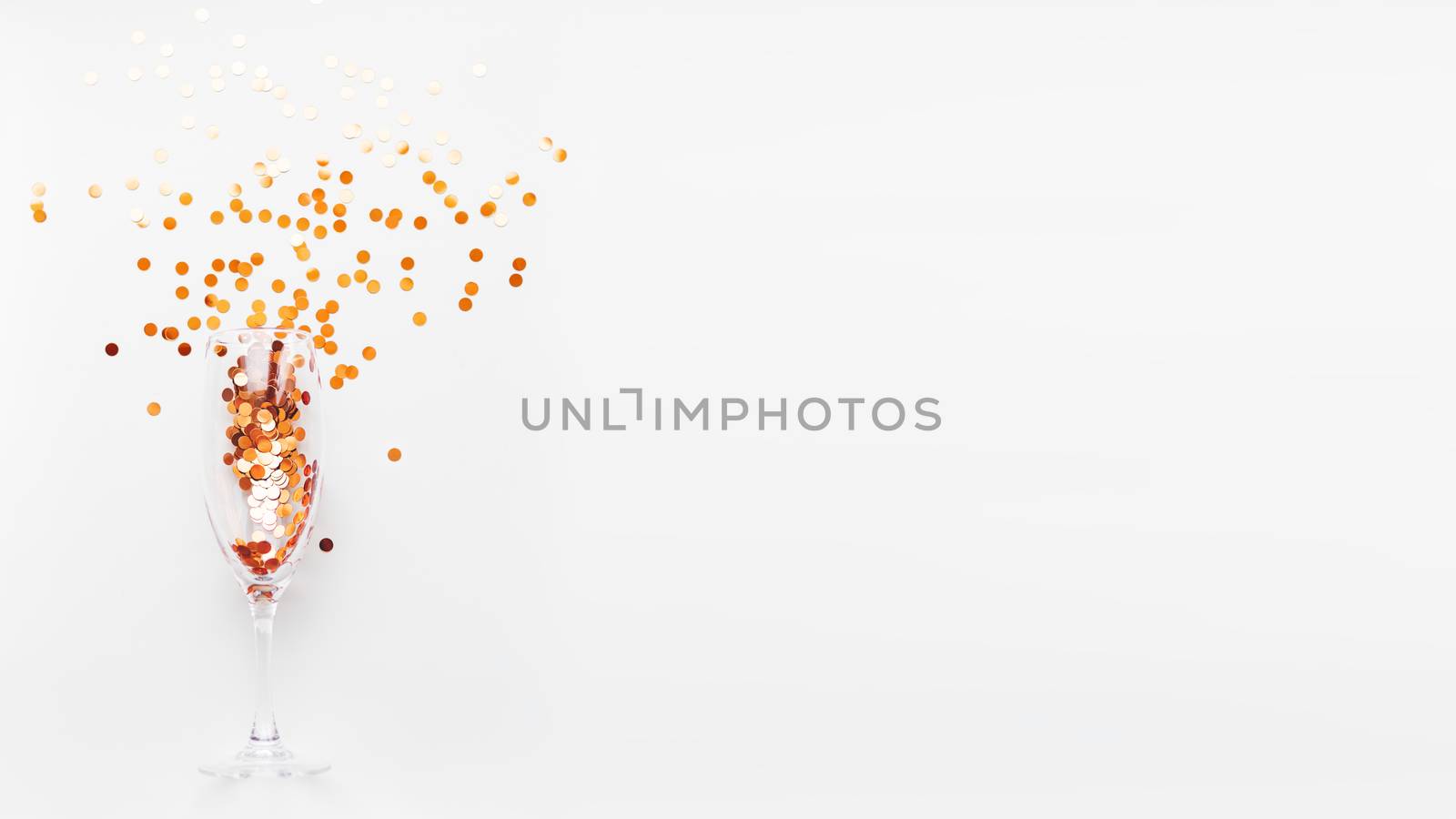 Transparent wine glass with golden spangles. Festive copy space with crockery on white background.