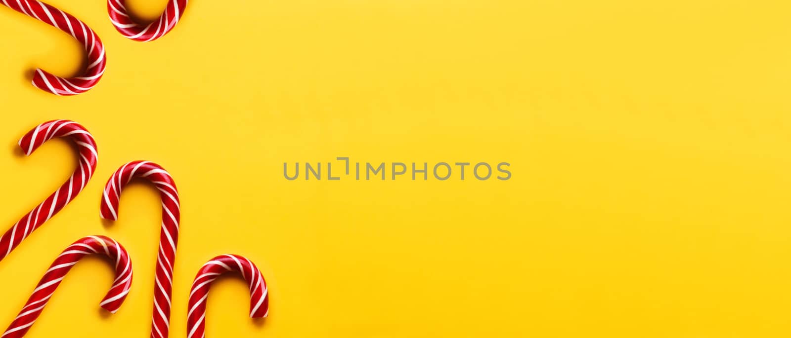 Banner with Christmas candy cones on yellow background. Colorful holiday sweets with bright copy space. Traditional dessert wtih red and white stripes.