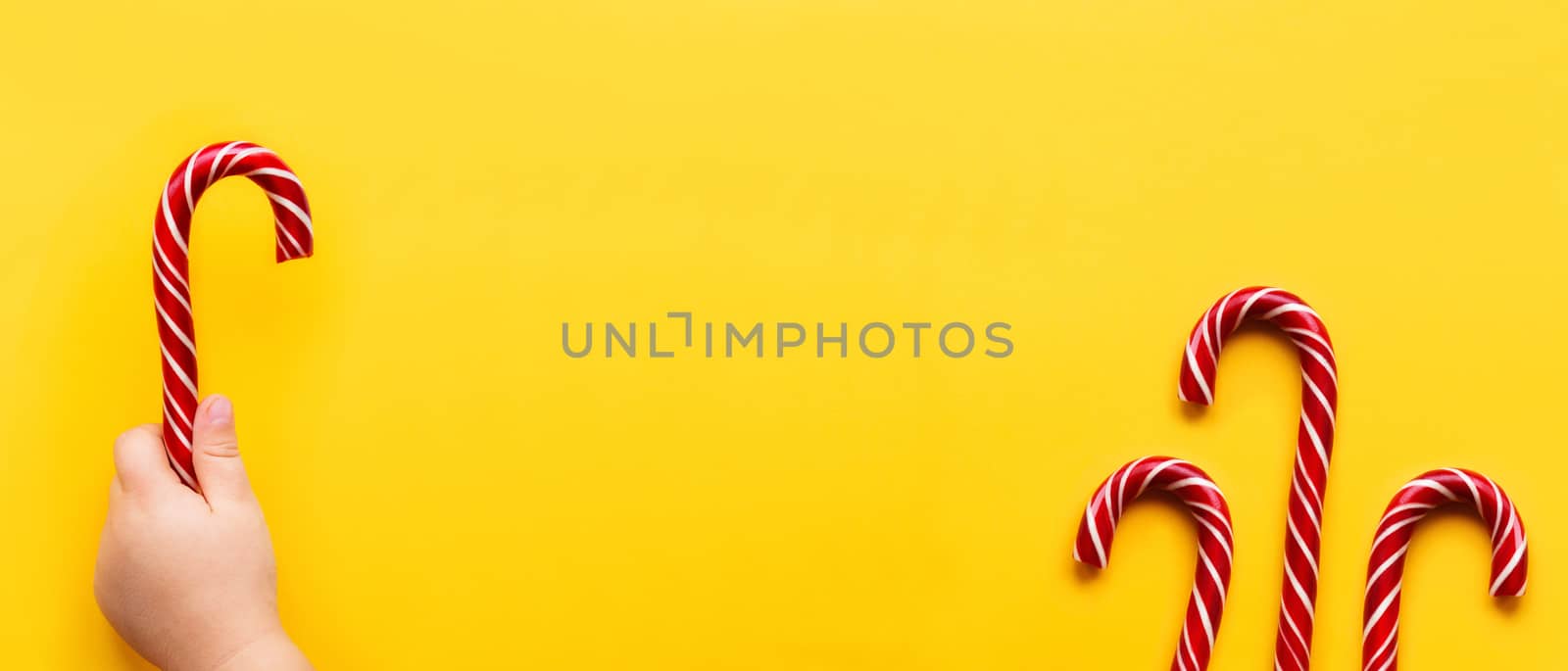 Three Christmas candy cones on yellow background. Colorful holiday sweets with bright copy space. Traditional dessert wtih red and white stripes.