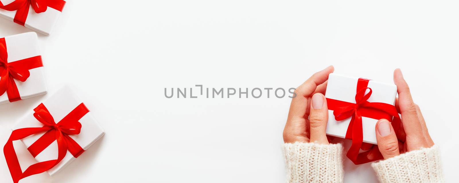 Woman holds a present in white wrapping paper on white backdrop. Holiday gifts with red ribbon and bow. Banner with copy space.