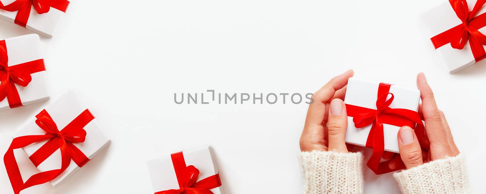 Woman holds a present in white wrapping paper on white backdrop. Holiday gifts with red ribbon and bow. Banner with copy space.