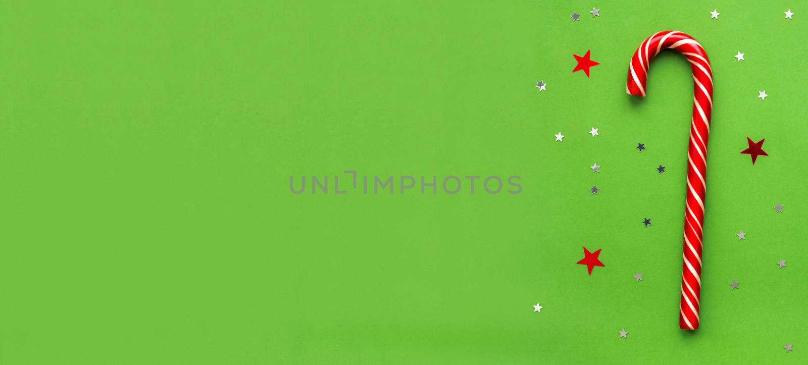 Christmas and New Year green background with traditional candy. Bright red and white lollipop with stars confetti. Top view, flat lay. Copy space.