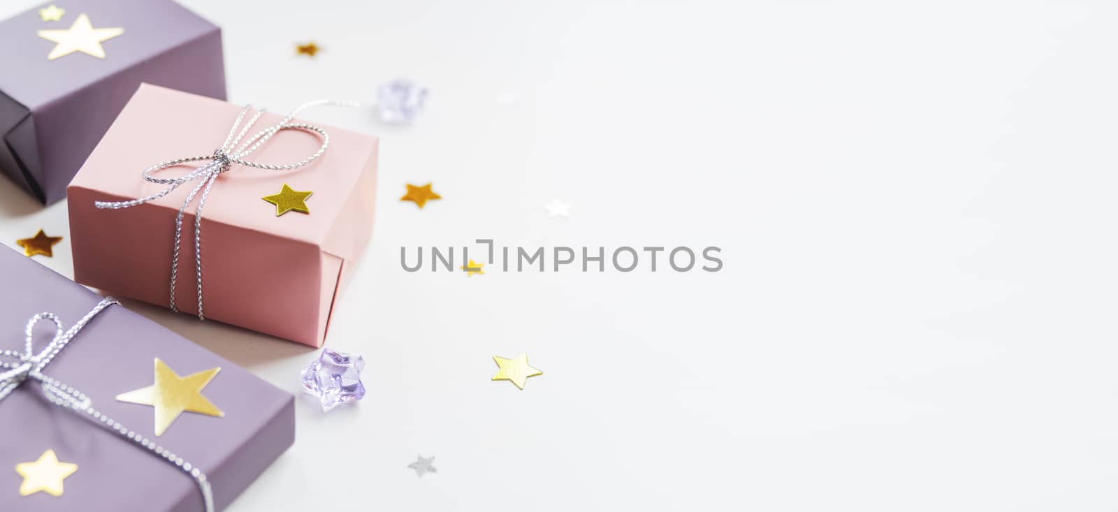 Banner with holiday presents. Gifts wrapped in pale pink and violet paper with silver ribbons and bow. Stars confetti and white copy space.