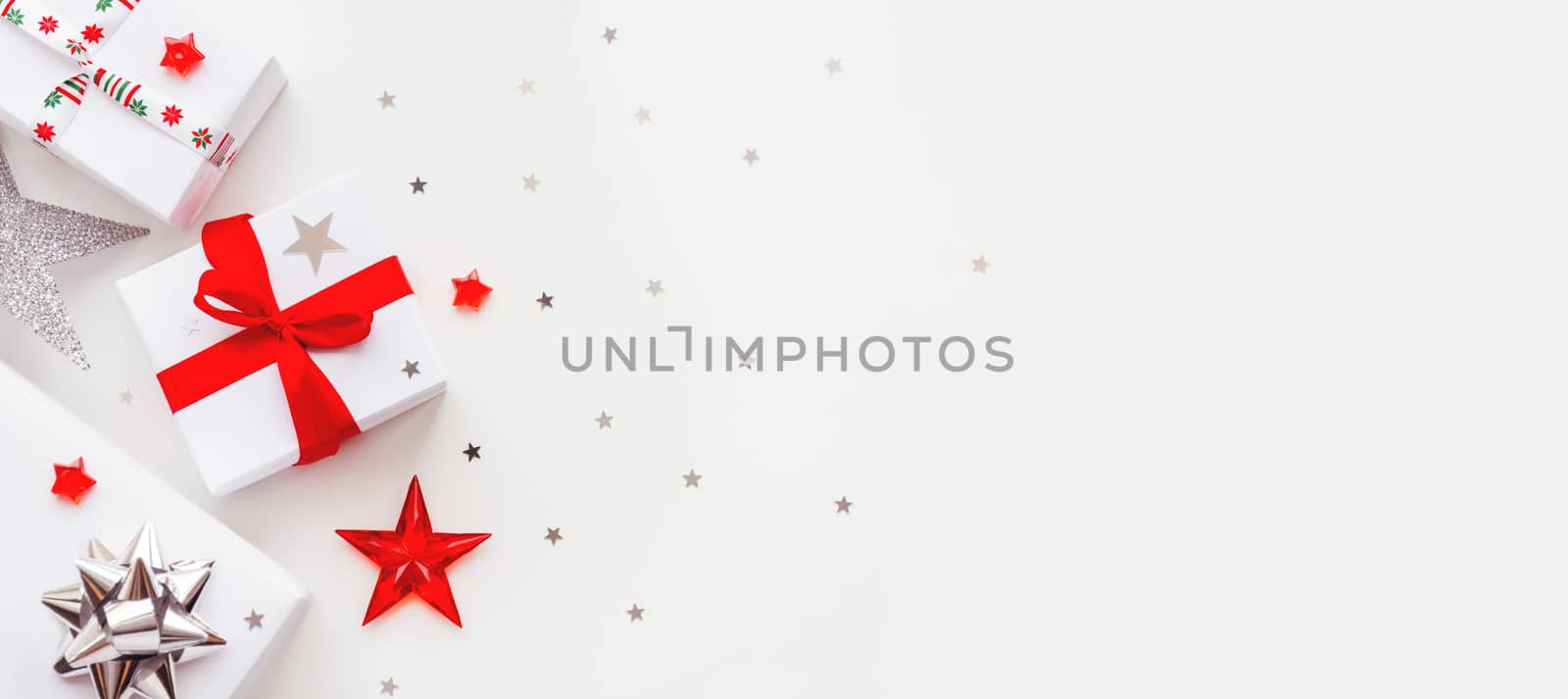 Christmas and New Year banner with presents in white wrapping paper. Holiday gifts with red and silver ribbon and bows. Copy space with silver star confetti.