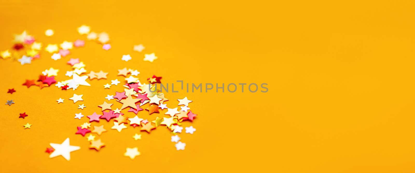 Yellow holiday background with colorful star confetti. Good background for Christmas and New Year cards.