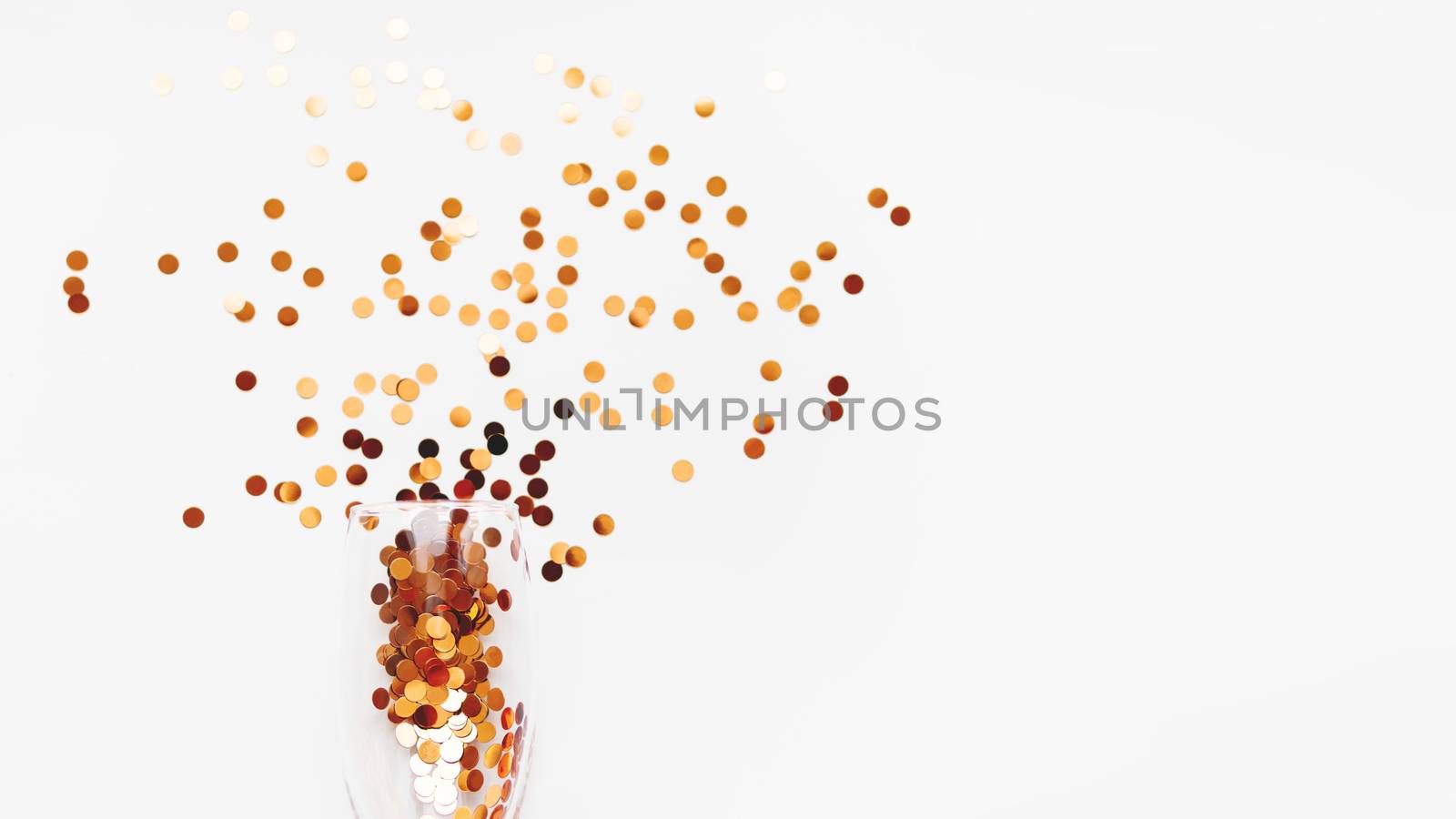 Transparent wine glass with golden spangles. Festive copy space with crockery on white background.