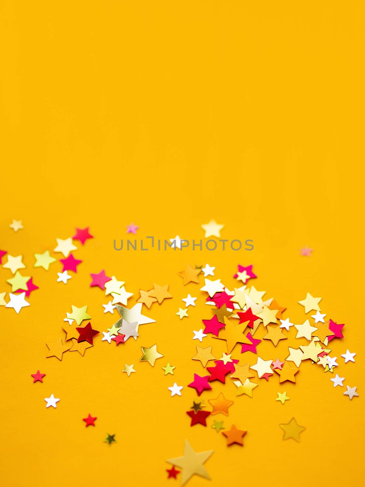 Yellow holiday background with colorful star confetti. Good background for Christmas and New Year cards.