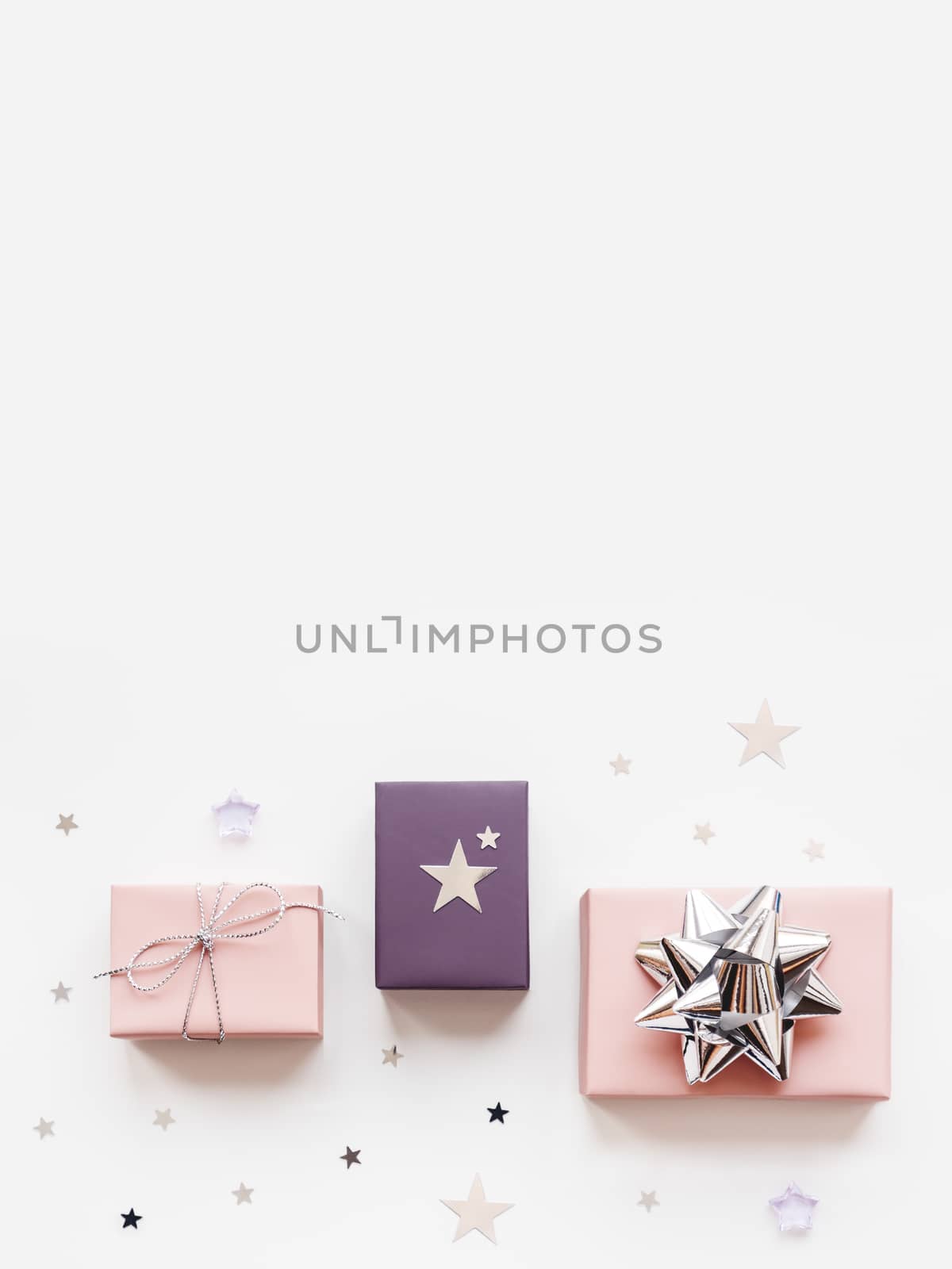 Banner with holiday presents. Gifts wrapped in pale pink and violet paper with silver ribbons and bow. Stars confetti and white copy space. Top view, flat lay.