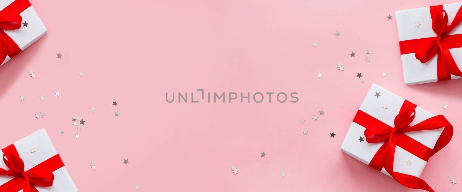 Banner with presents in white wrapping paper on pink backdrop with silver star confetti. Holiday gifts with red ribbon and bow. Top view, flat lay.