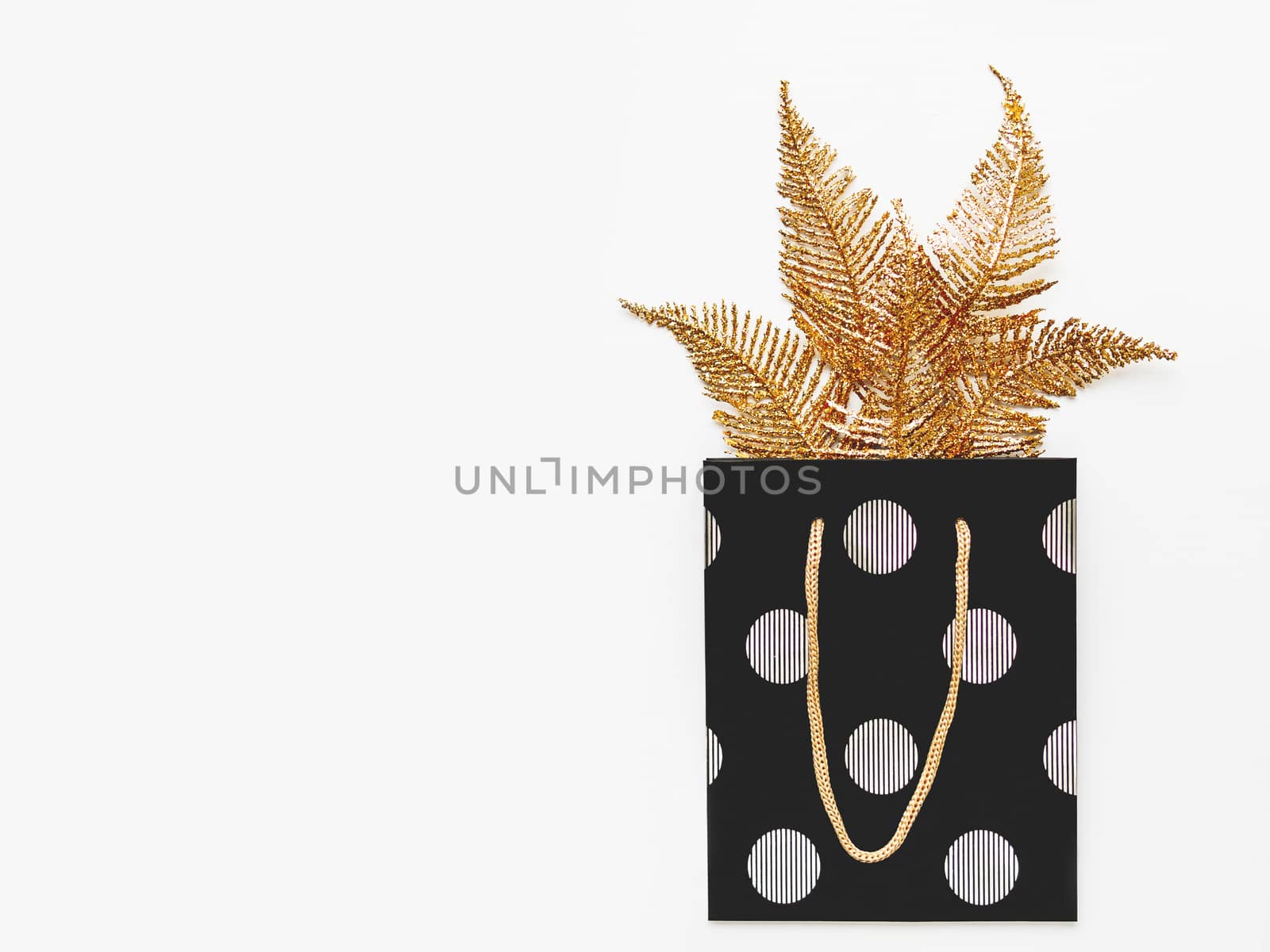 Bright golden feathers protrude from black gift bag with silver circles. New Year present with decorations for Christmas tree. Top view, flat lay.