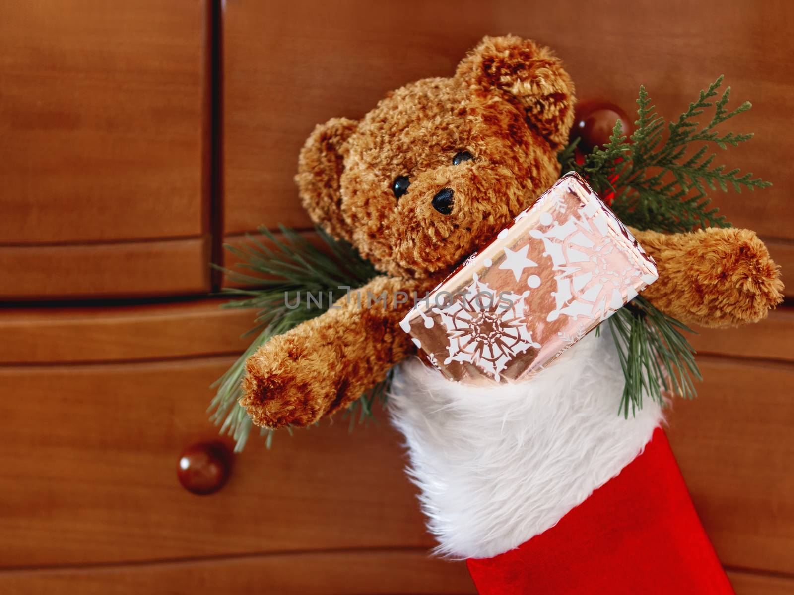 Brown teddy bear in red Santa Claus sock. Plush toy with Christmas present. New Year gift in bright golden paper.