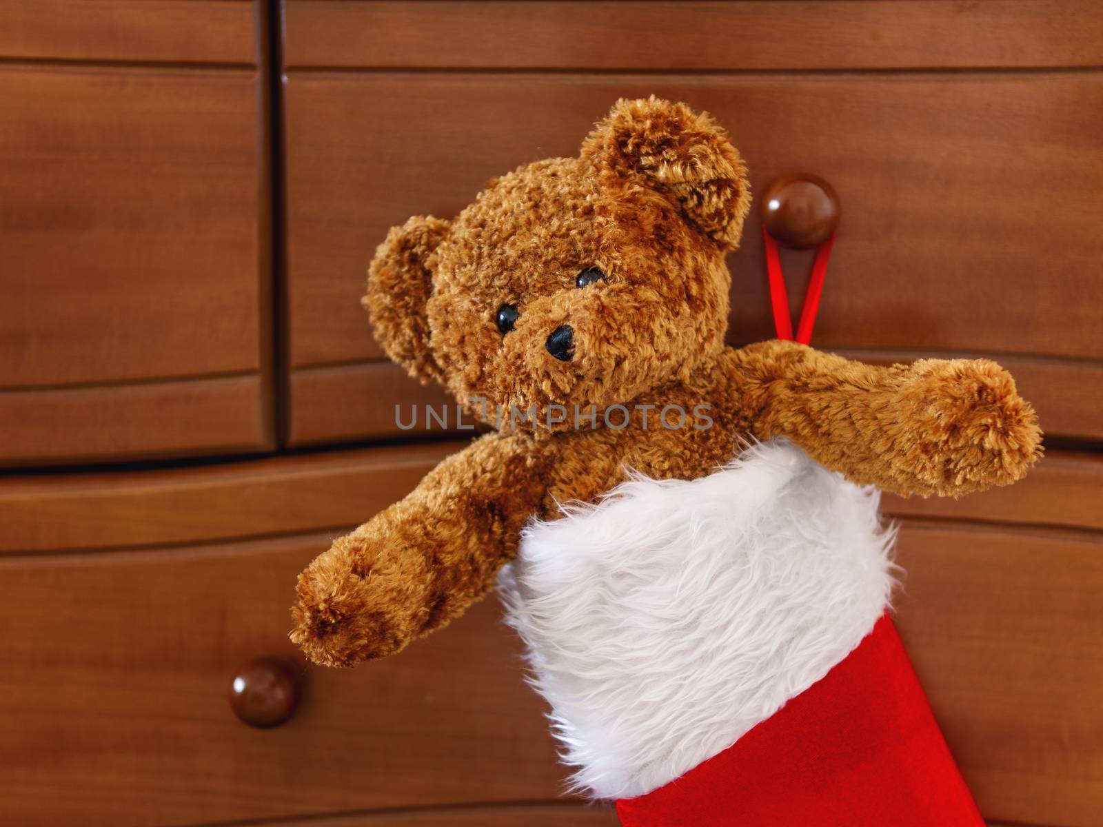 Brown teddy bear in red Santa Claus sock. Plush toy as Christmas present.