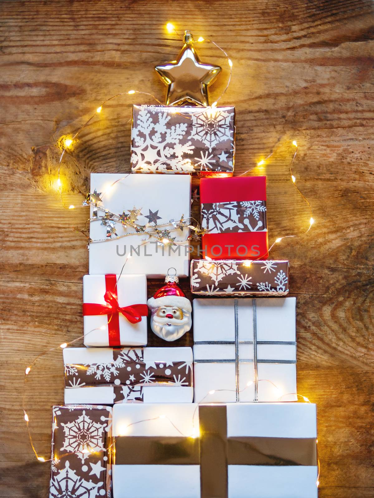New Year presents in shape of Christmas tree on shabby wooden background. Gifts in white and golden paper with bright ribbons and light bulbs.