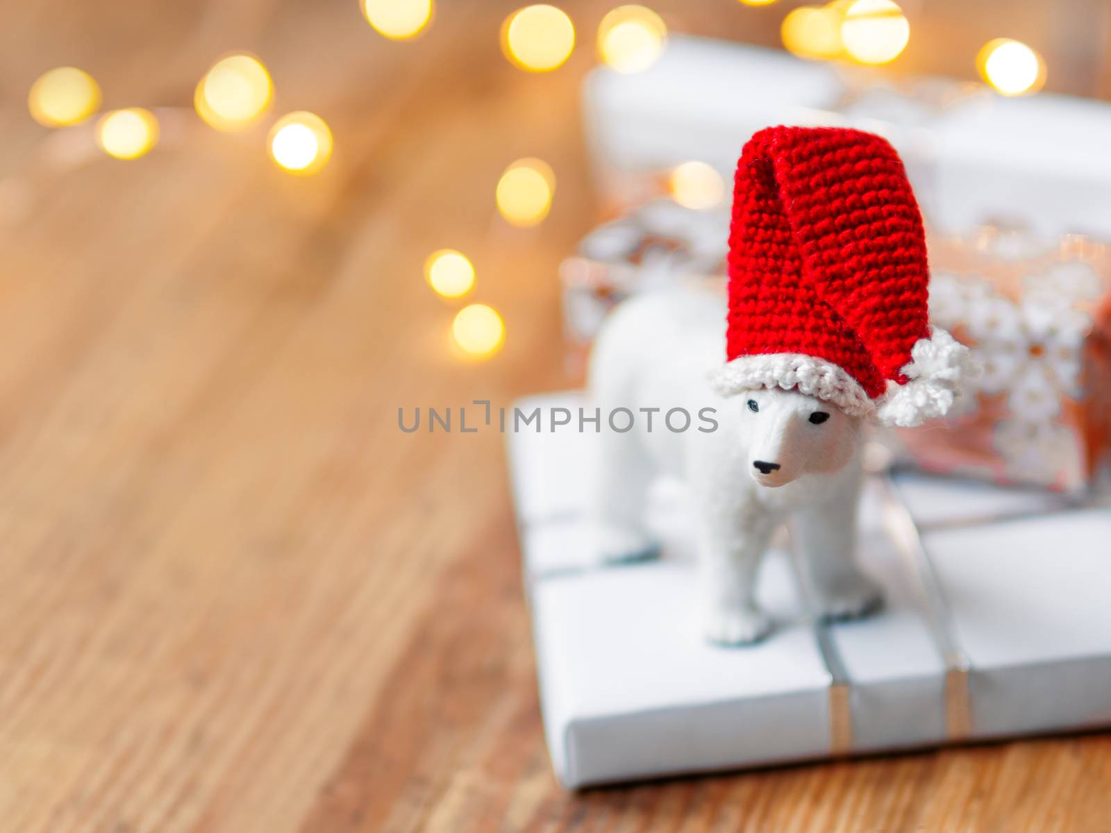 Christmas presents on shabby wooden background. Cute polar bear in Santa's hat standing on New Year gifts in white and golden paper.