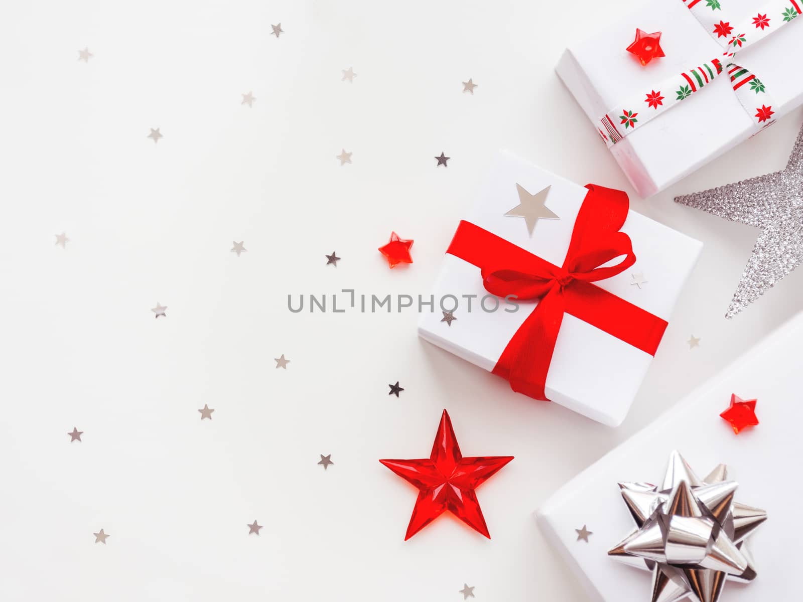 Christmas and New Year background with presents in white wrapping paper. Holiday gifts with red and silver ribbon and bows. Copy space with silver star confetti.