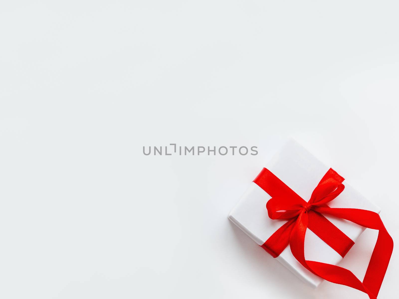 Present in white wrapping paper on white backdrop. Holiday gift with red ribbon and bow. Copy space.