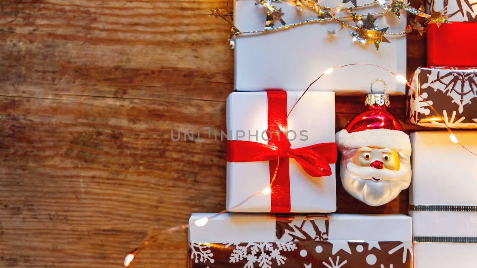Christmas presents on shabby wooden background. New Year gifts in white and golden paper with bright ribbons and light bulbs.