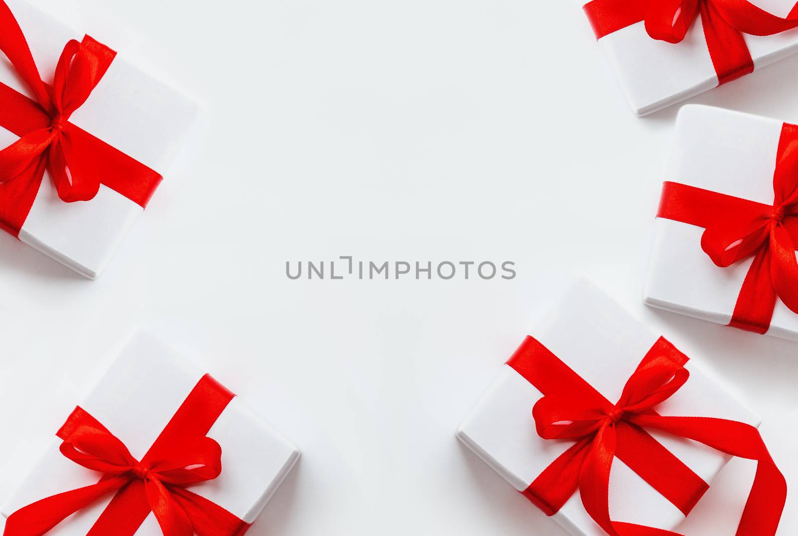 Presents in white wrapping paper on white backdrop. Holiday gifts with red ribbon and bow. Copy space.