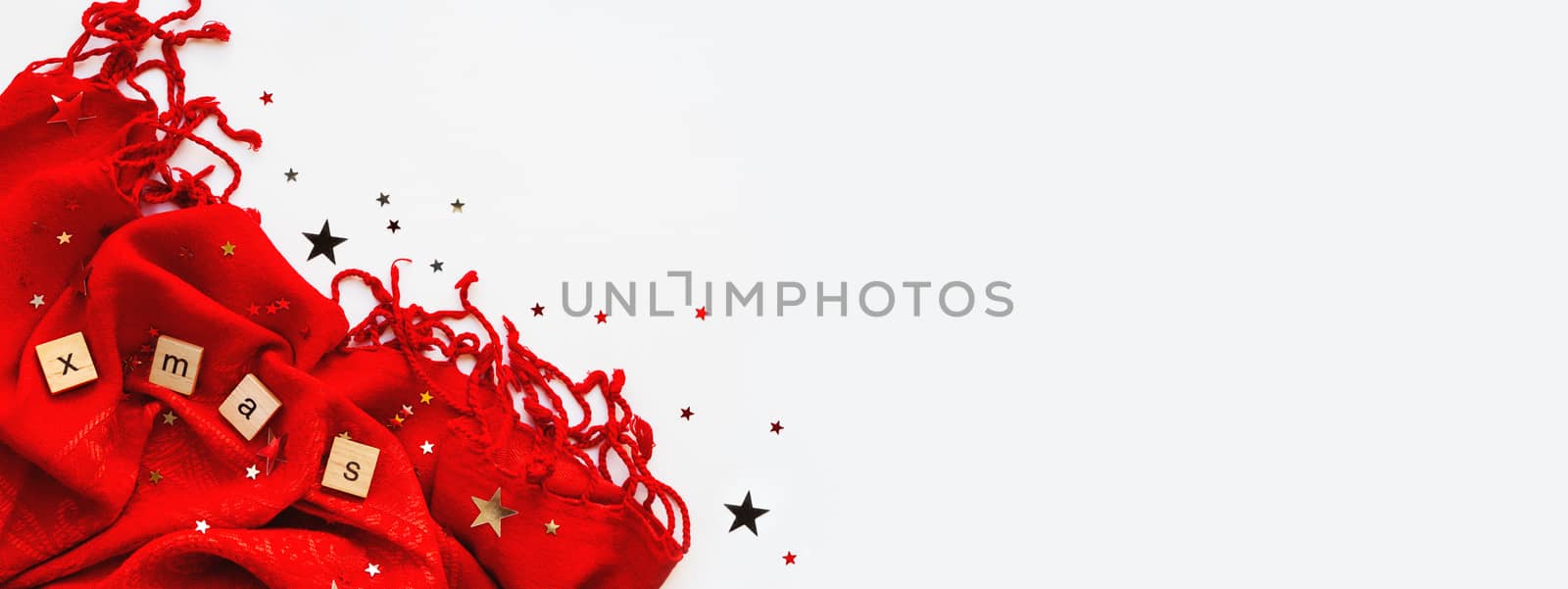 Christmas and New Year background. Bright red scarf with word XMAS and confetti on white background. Folded warm accessory with copy space.