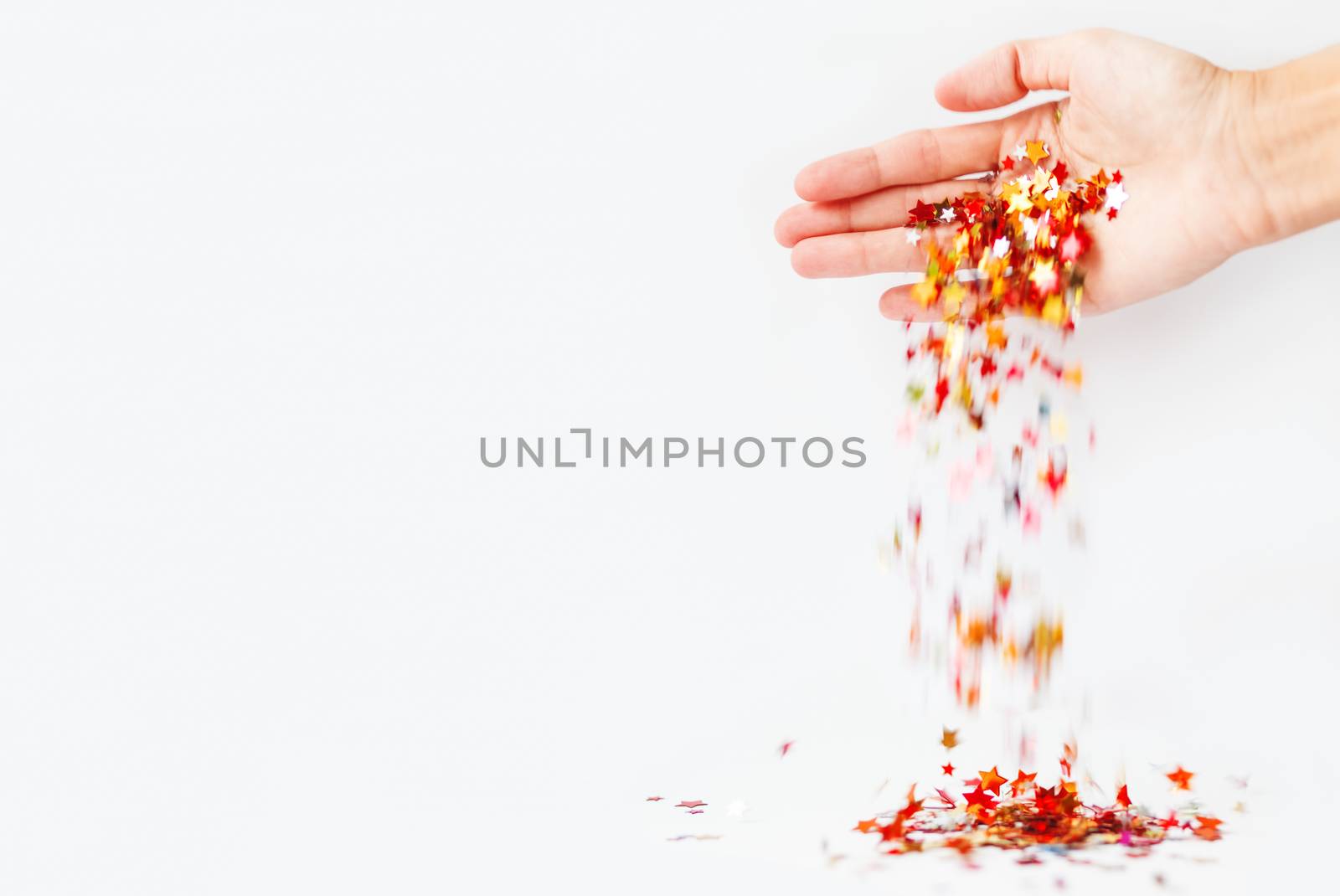 Confetti in shape of stars falls from woman's palm. Colorful spangles on white background with copy space.
