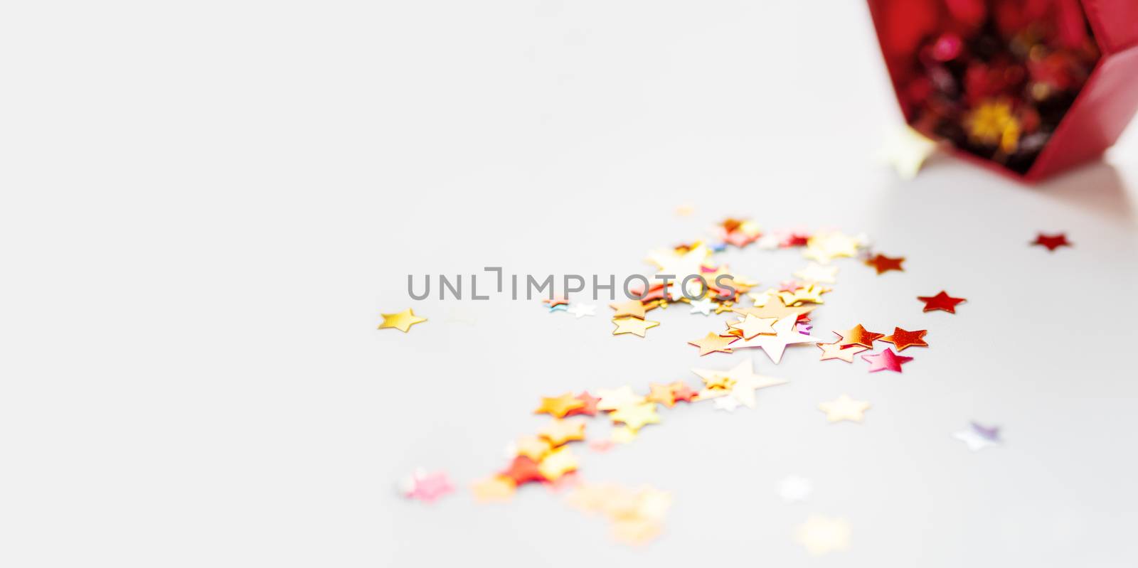 Banner with stars confetti which fallen from red sparkling box. Holiday decoration on white background.