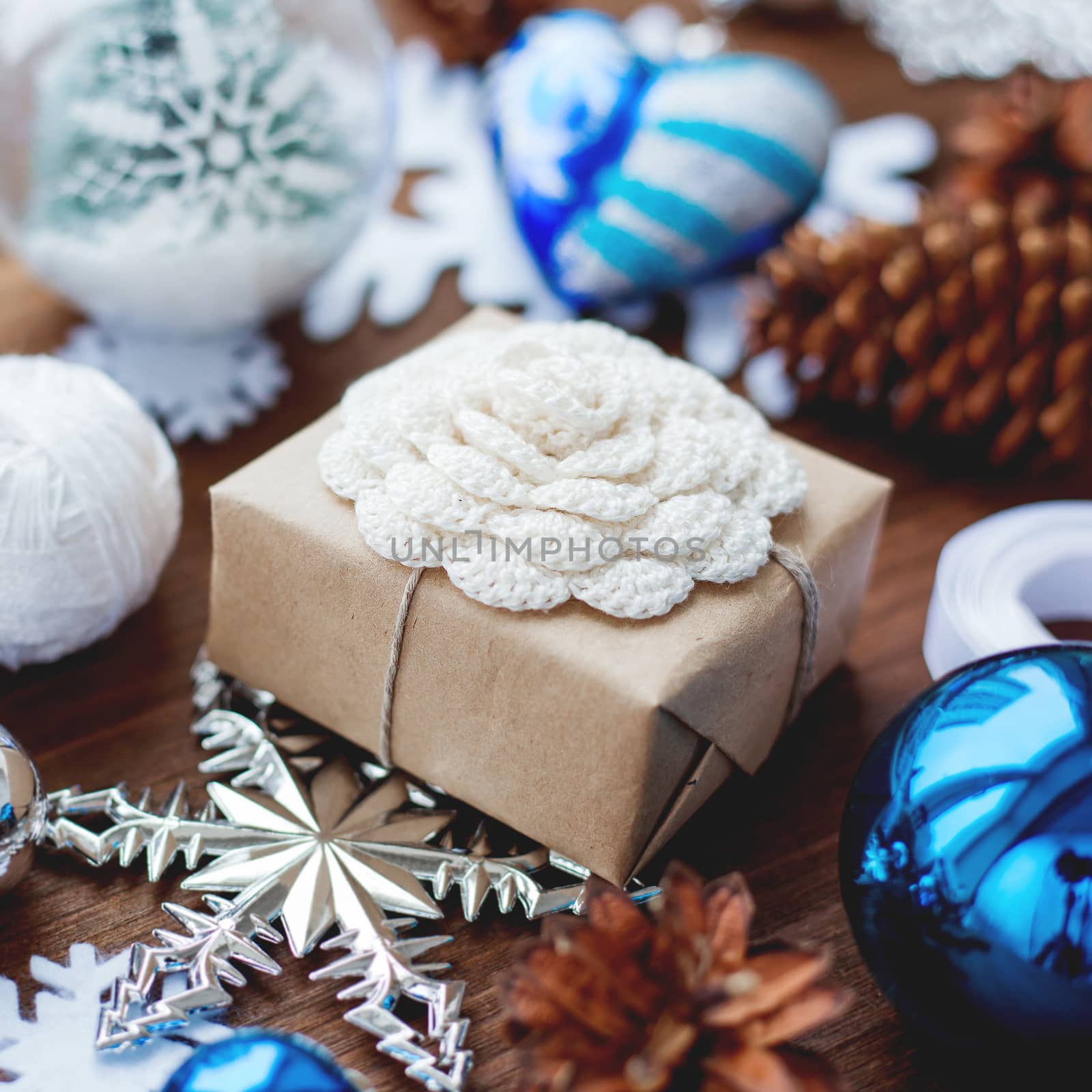 Christmas and New Year background with presents, ribbons, balls and different blue decorations on wooden background. Gift packed in craft paper with hand made crochet flower. DIY way to wrap a present. by aksenovko