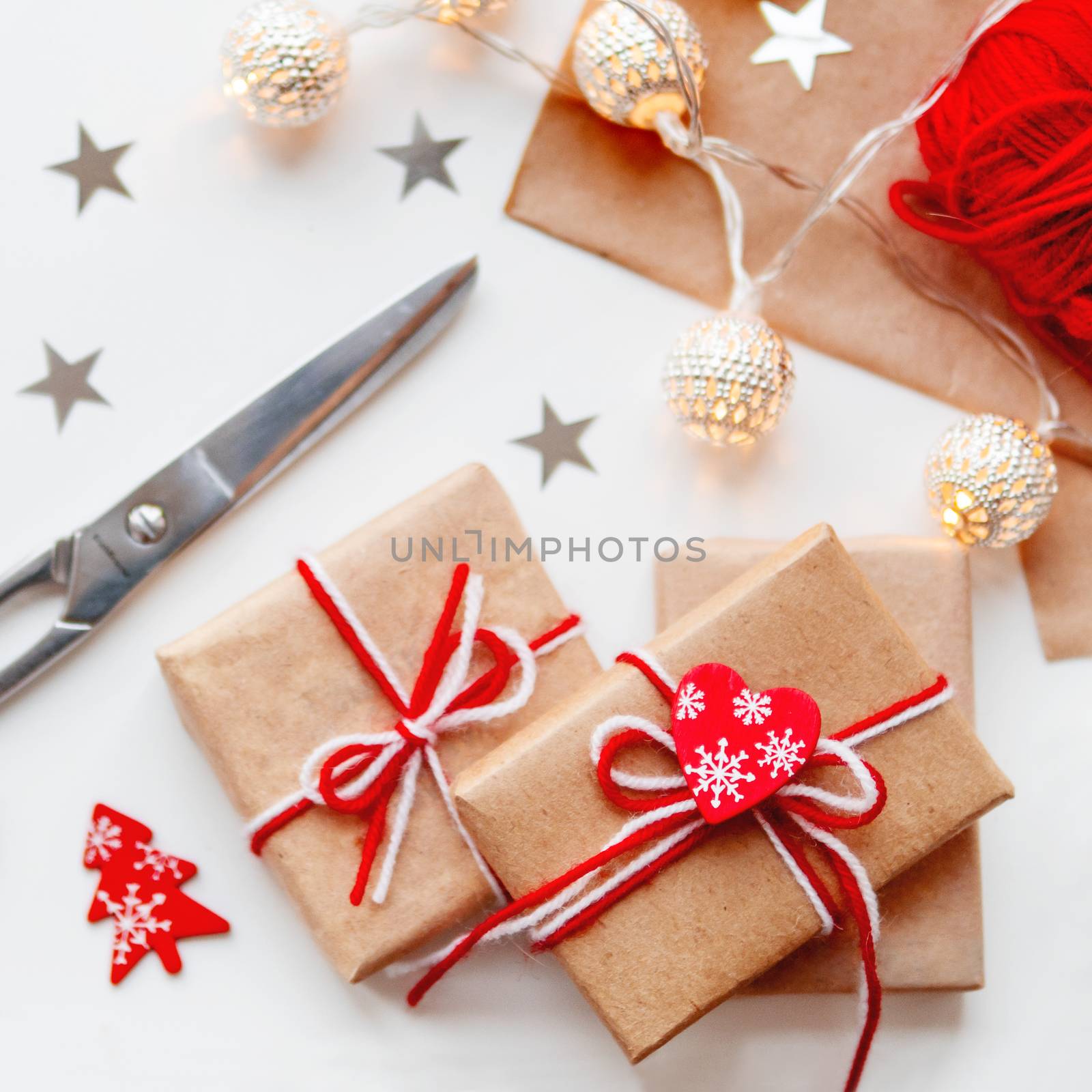 DIY presents wrapped in craft paper. Gifts tied with white and red threads with red heart symbol. Metal light bulbs with delicate pattern.