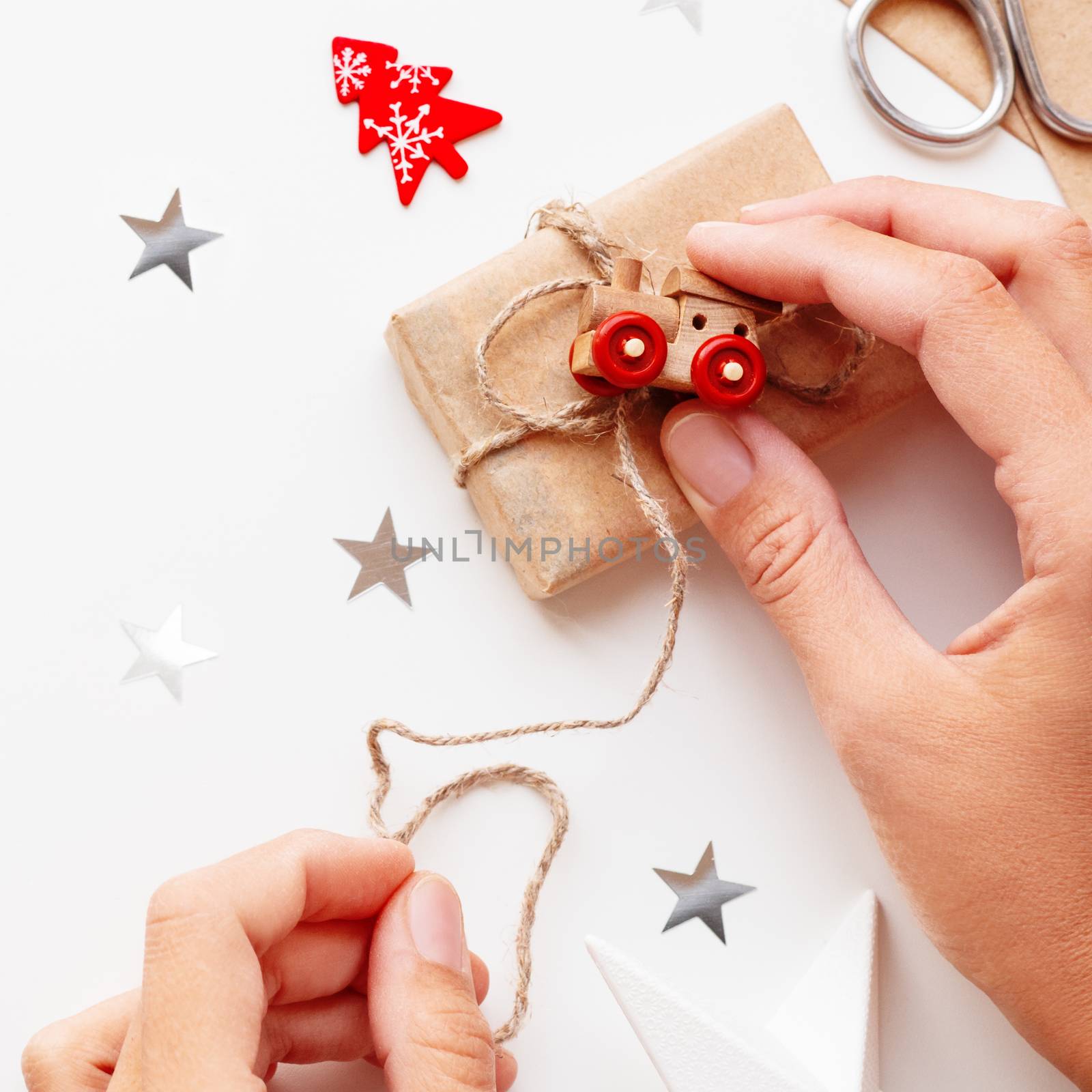Woman wrapping Christmas and New Year DIY presents in craft paper. Gift tied with toy train as decoration.