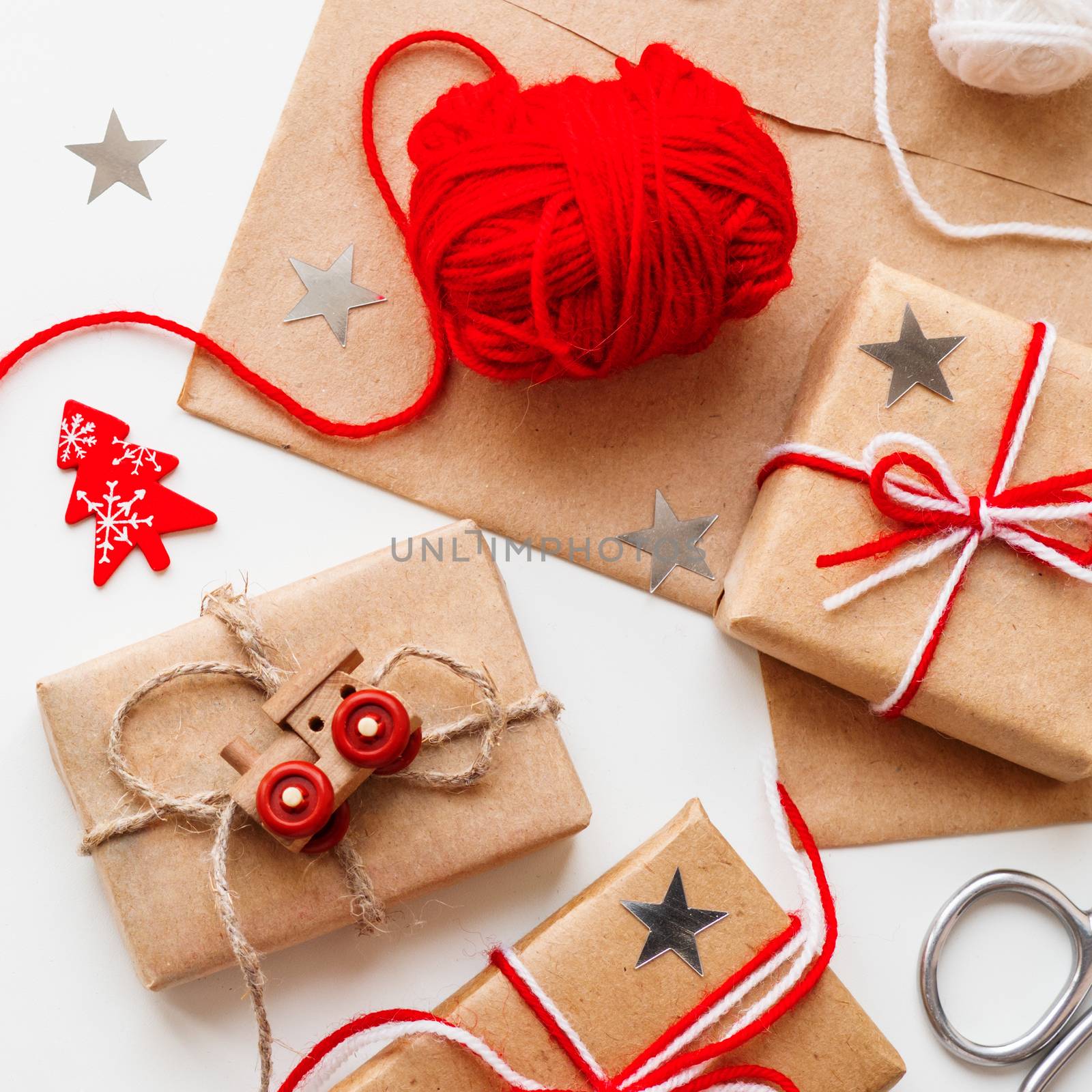 Christmas and New Year DIY presents in craft paper. Holiday gifts tied with white and red threads with toy train and red heart symbol as decoration.