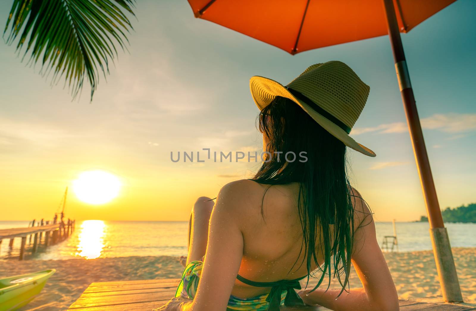 Sexy, enjoy and relax Caucasian woman wear bikini lying and sunbathing on sunbed at sand beach at paradise tropical island under beach umbrella at sunset. Summer vacation on the beach. Holiday travel.