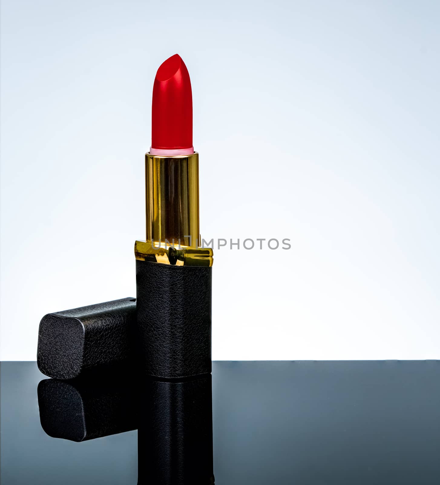 Red matte lipstick in gold and black tube package put on dark table isolated on white background in studio. Red lipstick with open cap. Makeup beauty cosmetic for confident fashion women. 