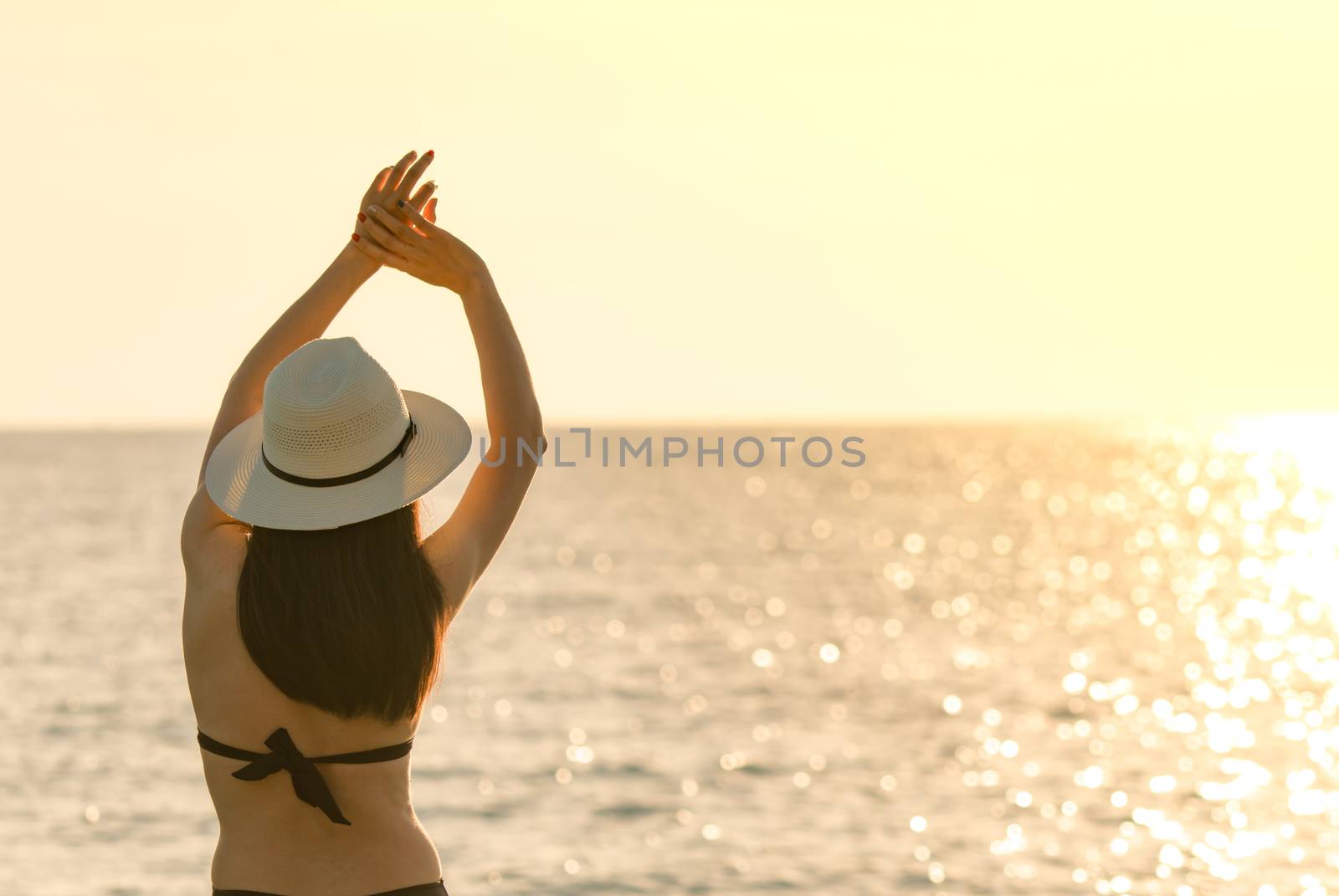 Back view of happy young Asian woman in black swimsuit and straw hat relax and enjoy holiday at tropical paradise beach at sunset. Girl in summer vacation fashion. Beauty sexy model. Elegant lifestyle