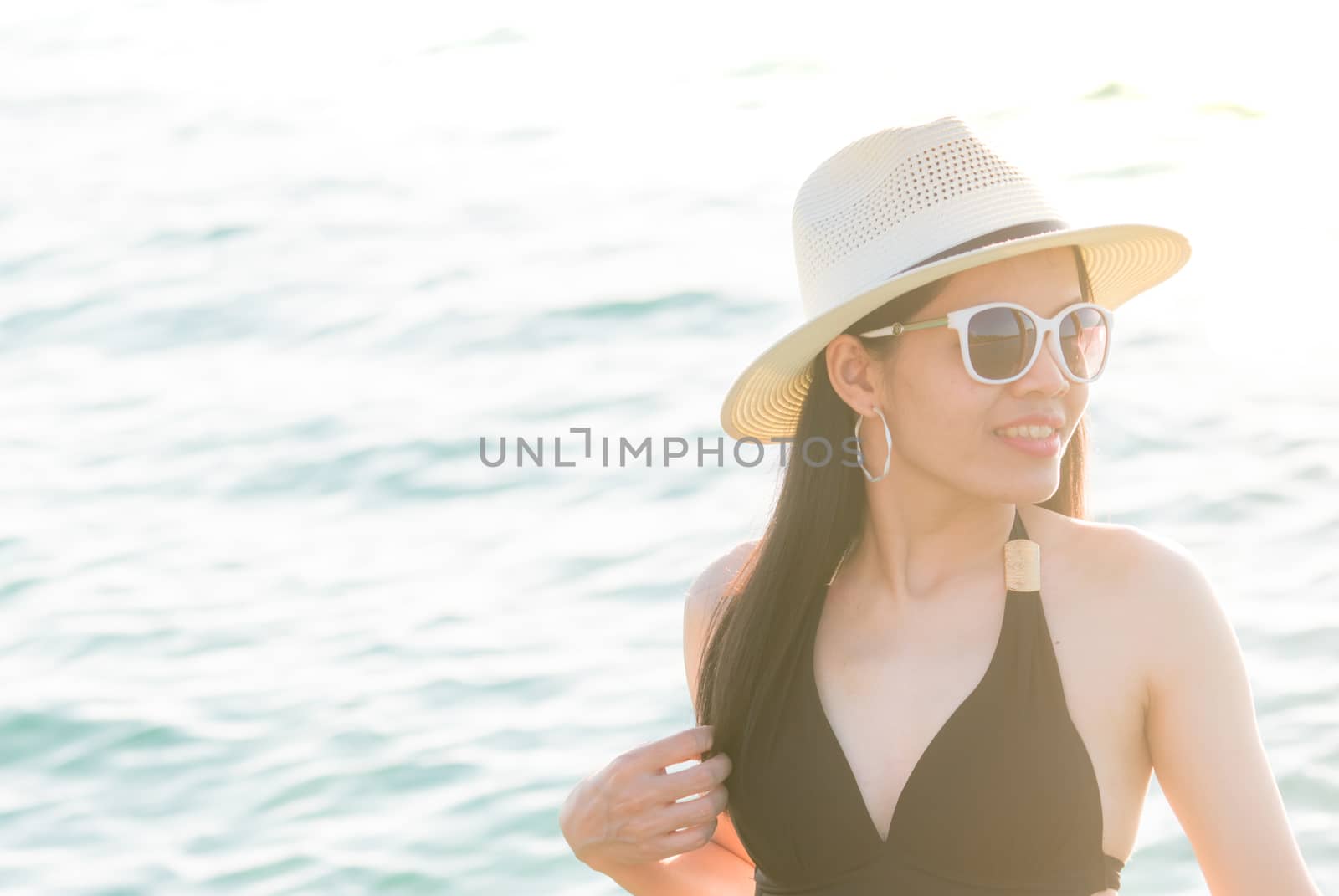 Sexy woman wear black swimwear, straw hat, and sunglasses relaxing and enjoy holiday at tropical paradise beach on sunny day. Girl in summer vacation. Holiday travel. Summer vibes. Elegant lifestyle.