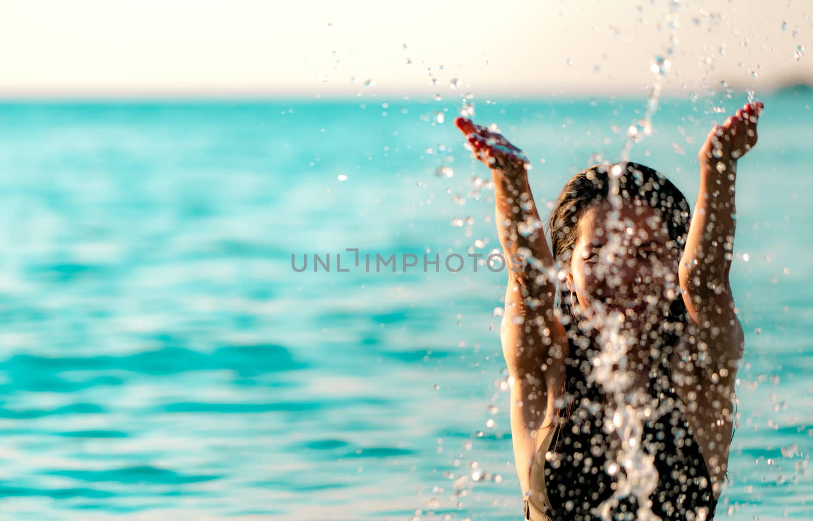 Happy young Asian woman in black swimsuit relax and enjoy holiday at tropical paradise beach. Girl in summer vacation splash water in the sea. Sexy model. Sexy woman in black bikini. Summer vibes.   