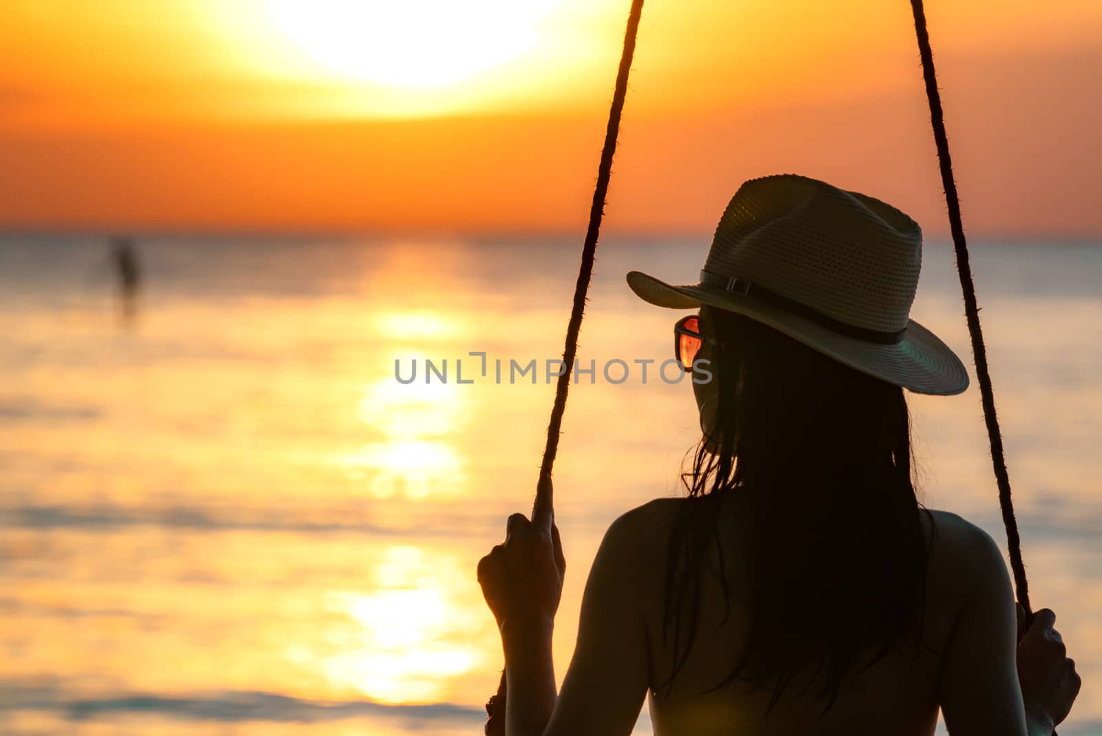 Silhouette woman wear bikini and straw hat swing the swings at t by Fahroni