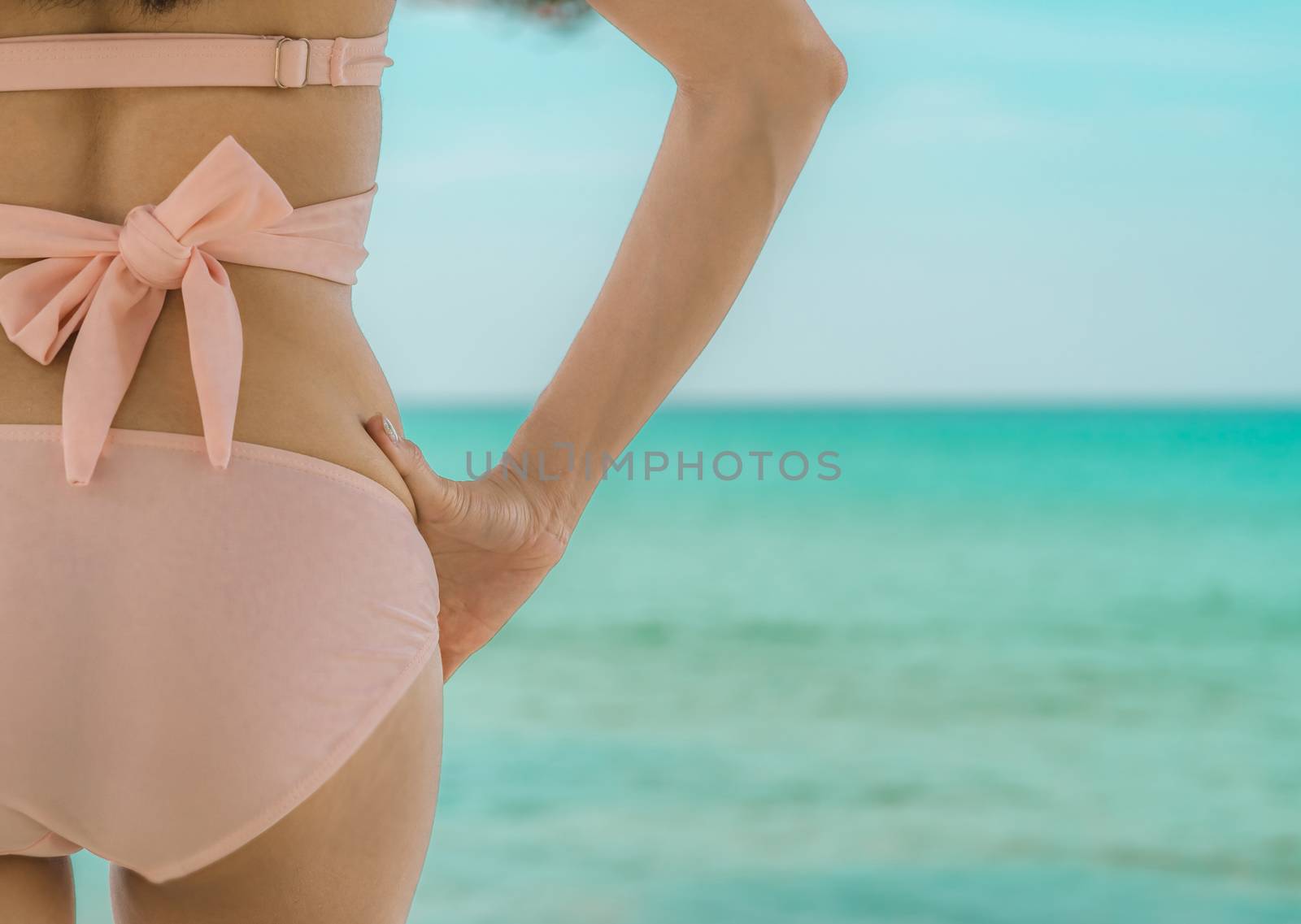 Back view of sexy adult Asian woman wear pink bikini relaxing and enjoy holiday at tropical paradise beach. Girl in summer vacation fashion. Summer vibes. Summer time. Woman enjoy swimming in the sea.