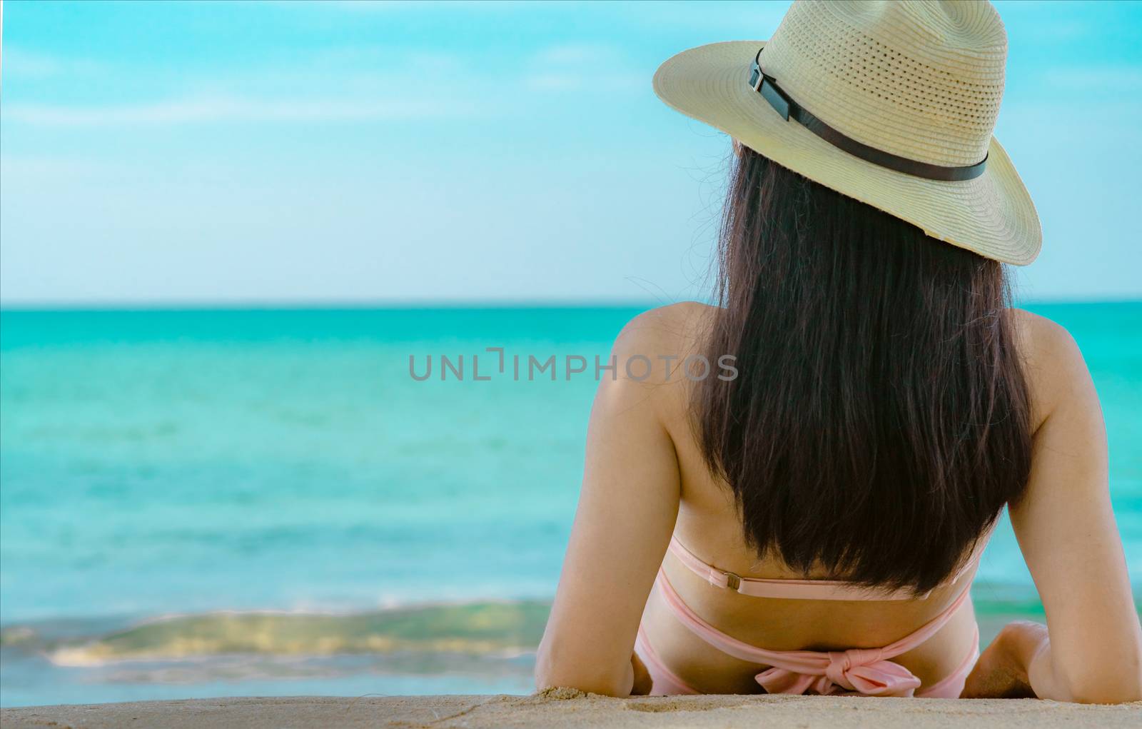 Back view of happy young Asian woman in pink swimsuit and straw hat relax and enjoy holiday at tropical paradise beach at sunset. Girl in summer vacation fashion. Beauty sexy model. Summer vibes.