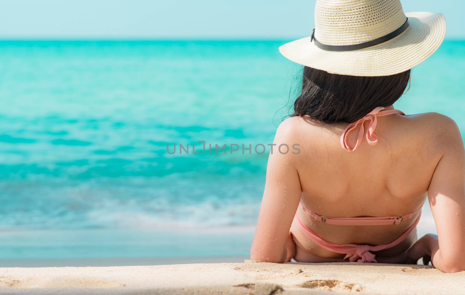 Back view of happy young Asian woman in pink swimsuit and straw hat relax and enjoy holiday at tropical paradise beach at sunset. Girl in summer vacation fashion. Beauty sexy model. Summer vibes.